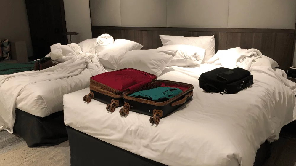 messy hotel beds with suit cases on the bed