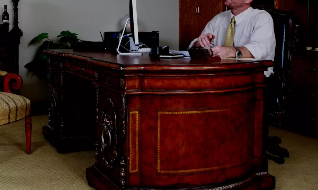 man sat at large mahogany desk in office